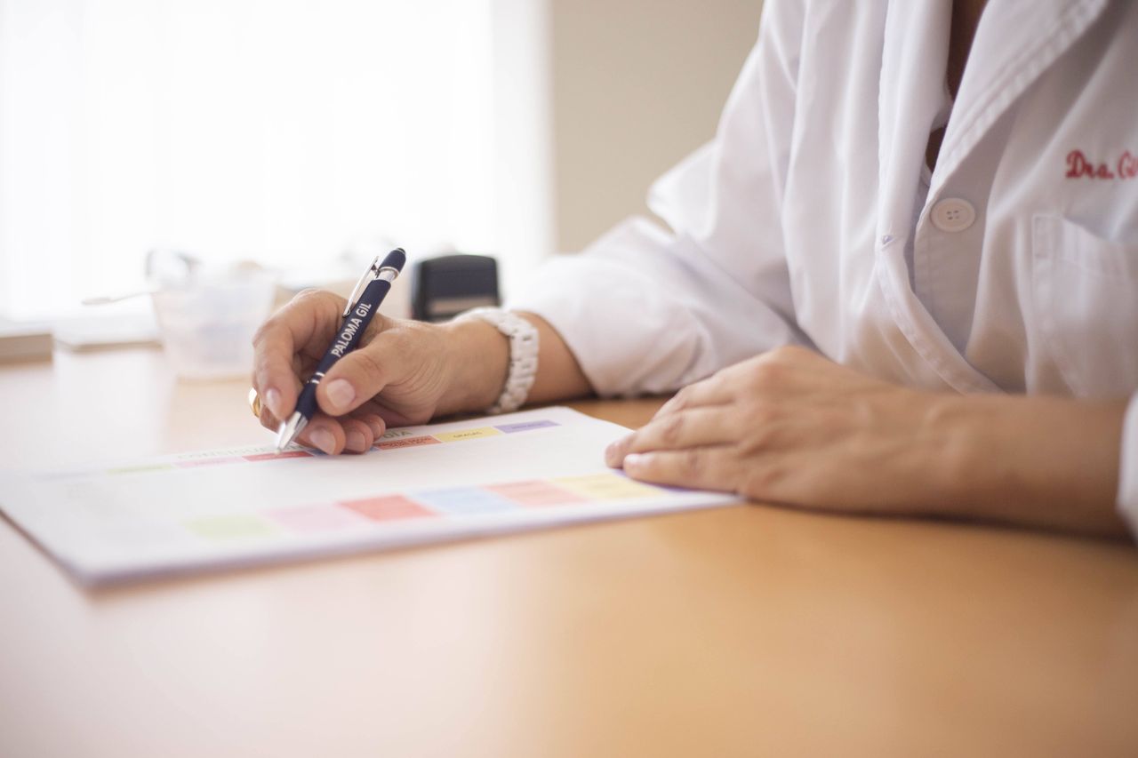 about-01 Close-up of a female doctor writing a prescription at a desk in an office setting.